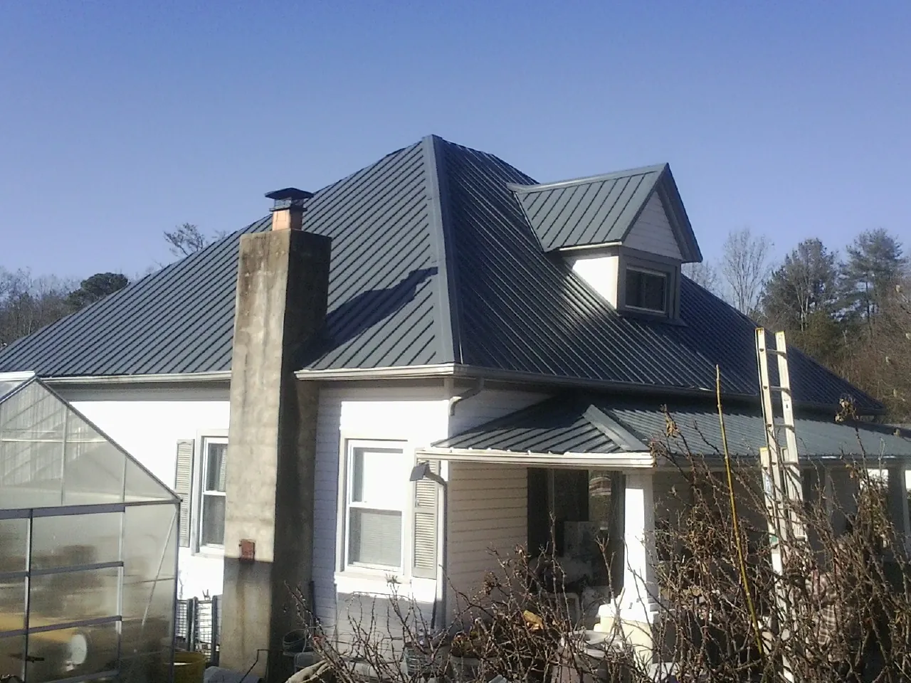 Dark blue standing seam metal roof on a white farmhouse with dormer — Slate & Tile Roof Repair by Roofing Brothers in Glenville