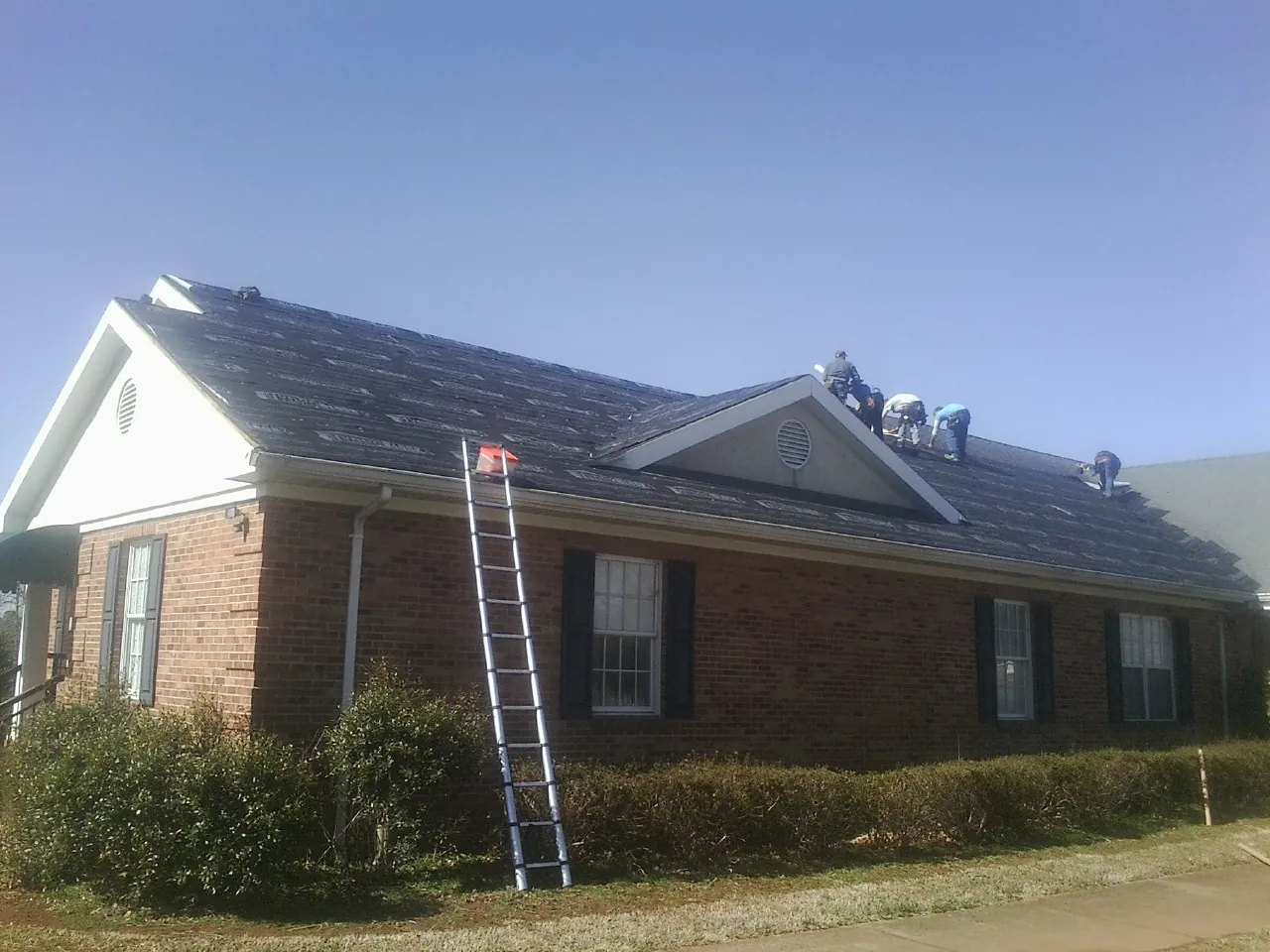 Crew tearing shingles off a brick ranch roof with a ladder set — Emergency Roof Repair work by our crew in Glenville