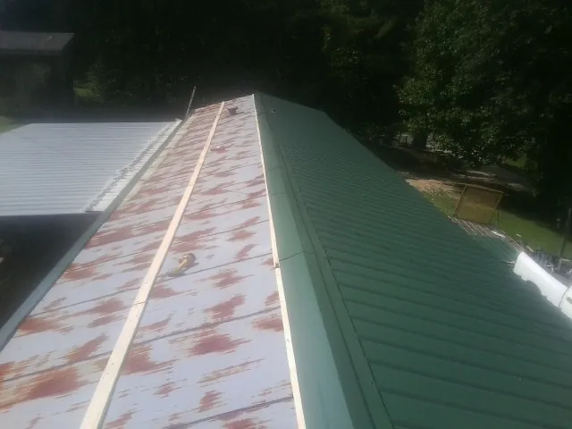 Old rusted panels beside newly installed green metal roofing — Wind Damage Roof Repair by Roofing Brothers in Glenville