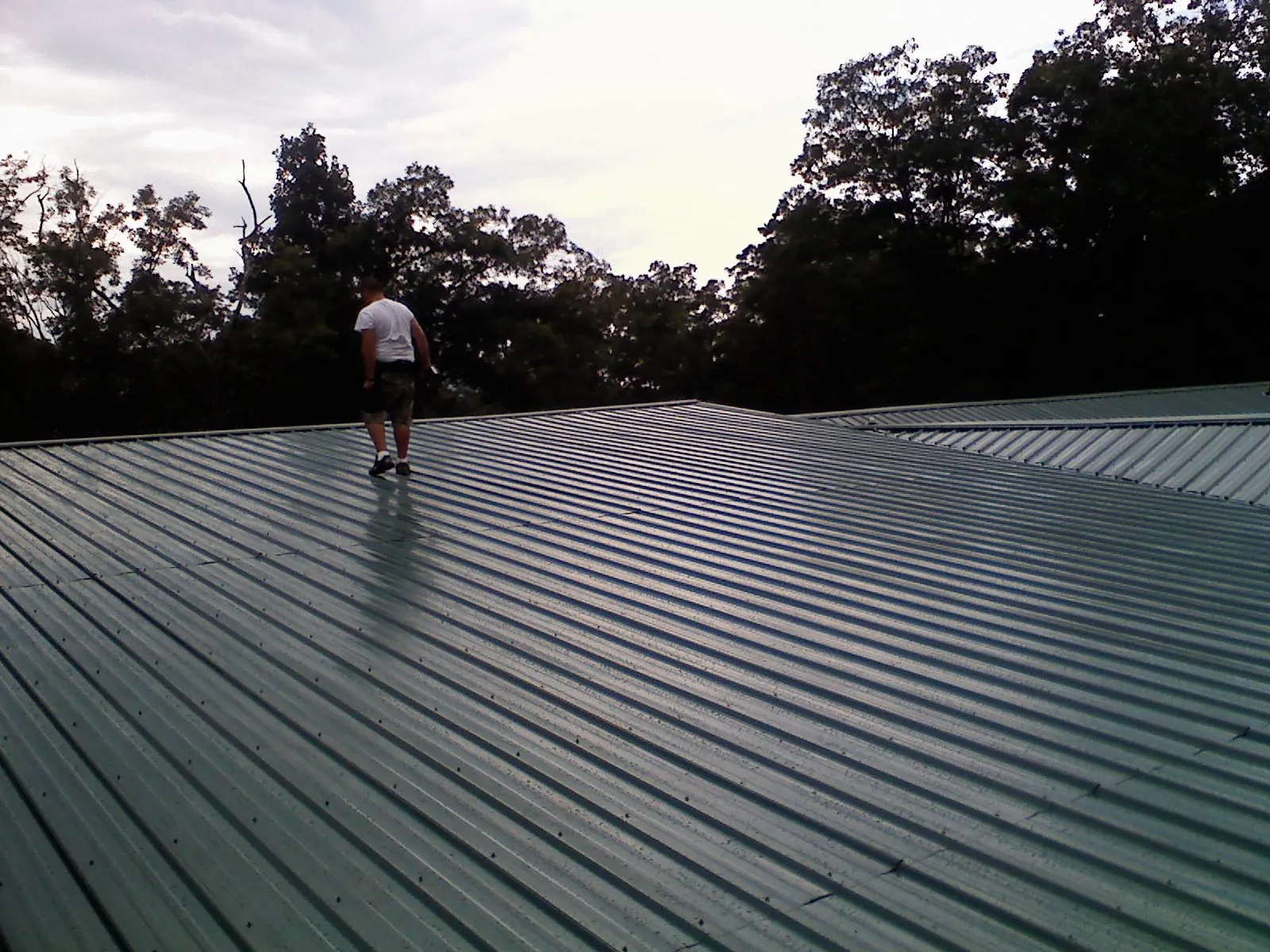 Roofer walking a wide expanse of new green metal roofing in Glenville