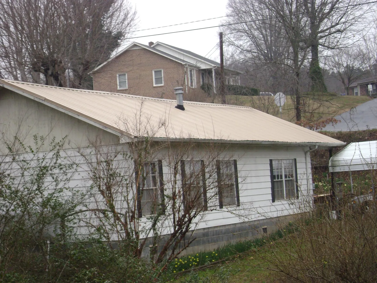 Tan metal roof on a white sided house set into a hillside — Commercial Roofing by Roofing Brothers in Glenville